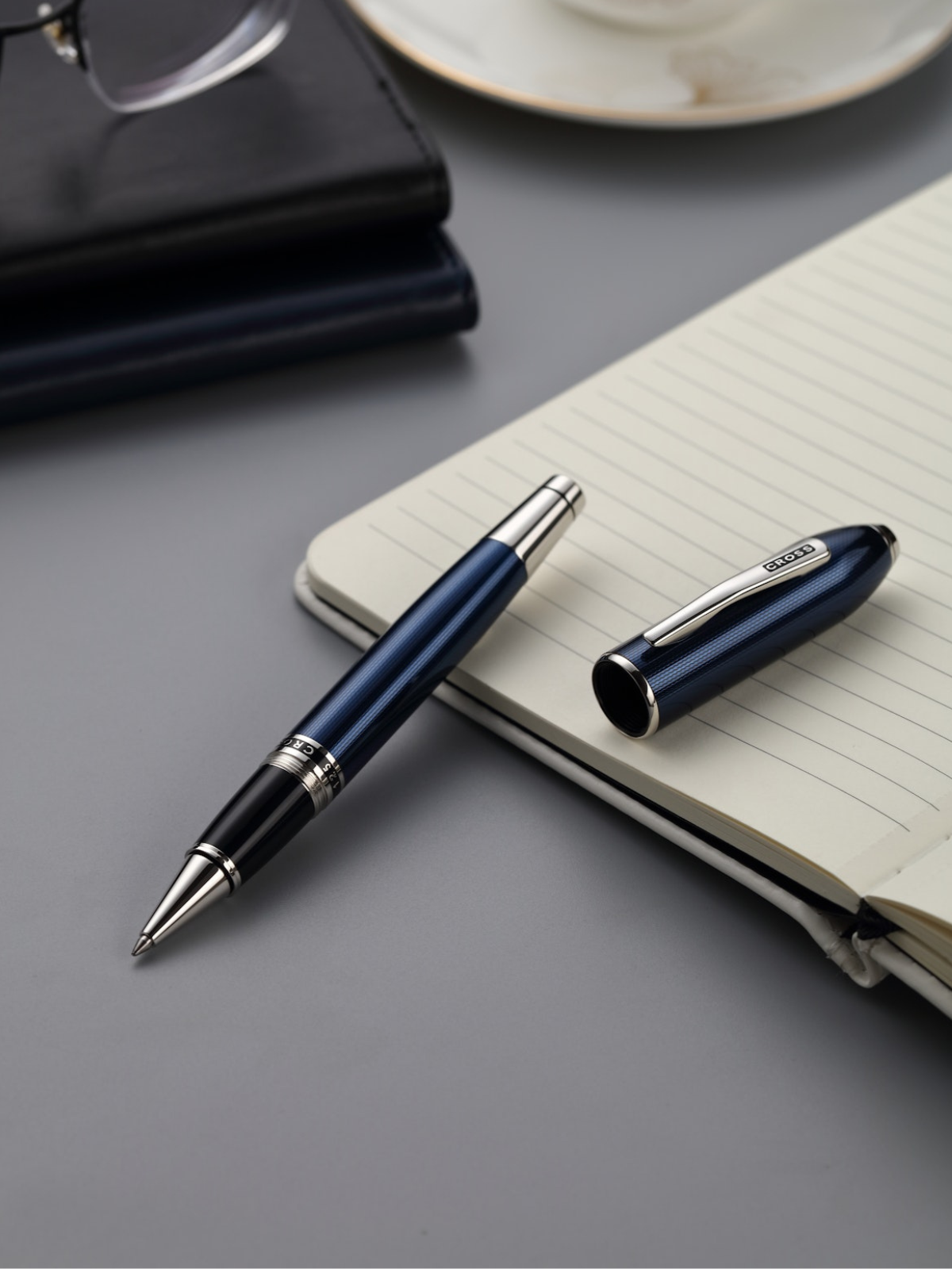 Blue pen with silver accents on a gray surface next to an open notebook